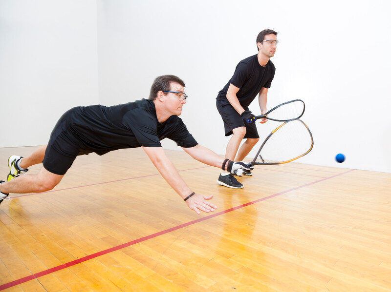 Two men playing racquetball on court. Shot at 1/100 of a second shutter speed to create a slight blurred motion to reveal the fast motion of racquetball.