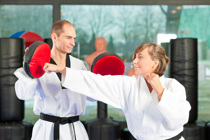 People in a gym in martial arts training exercising Taekwondo, both have a black belt