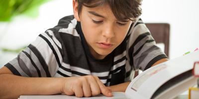 Reversing Learning Loss a concentrated boy reading a large book indoors
