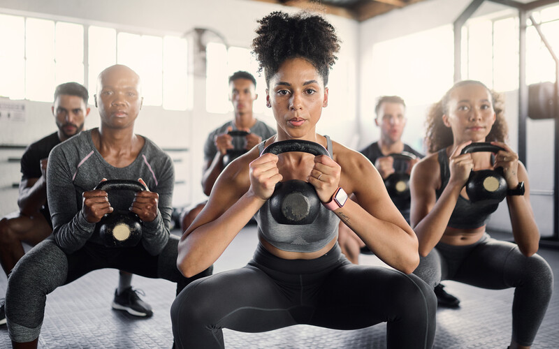 Fitness, kettle bell and gym class with a black woman coach training an athlete group in an exercise center. Workout, health and wellness with a man and woman team exercising in a sports facility